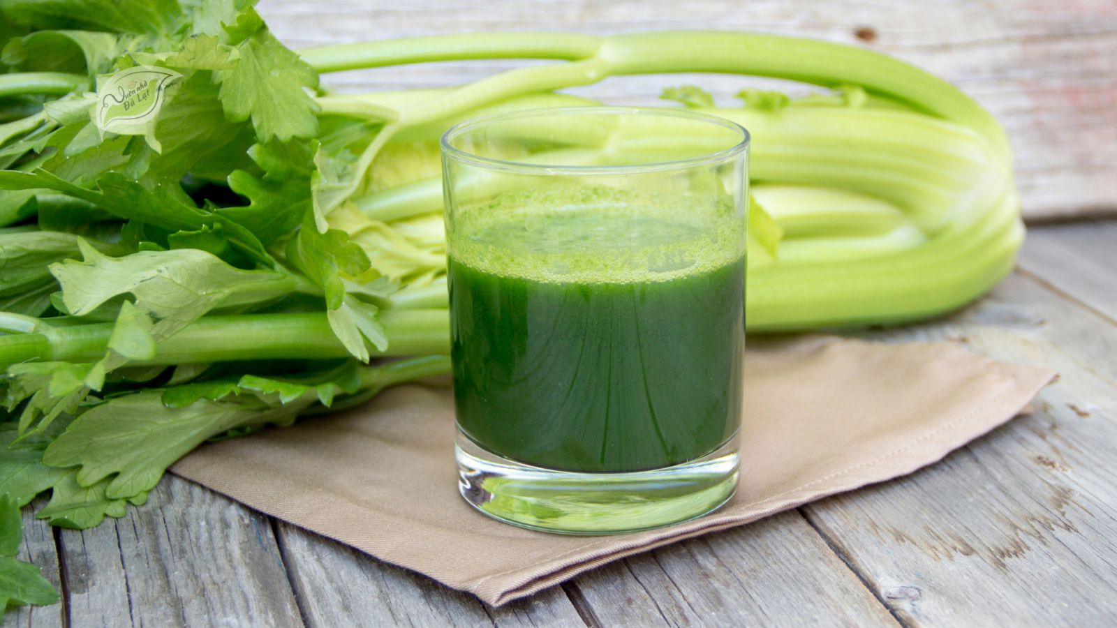 Ly nước bột cần tây xanh nhạt trên bàn sáng, bên cạnh ánh nắng dịu và tạp chí chăm sóc sức khỏe.”